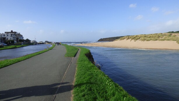Una carretera costera con un camino de hierba a lo largo de un río, que desemboca en una playa de arena.