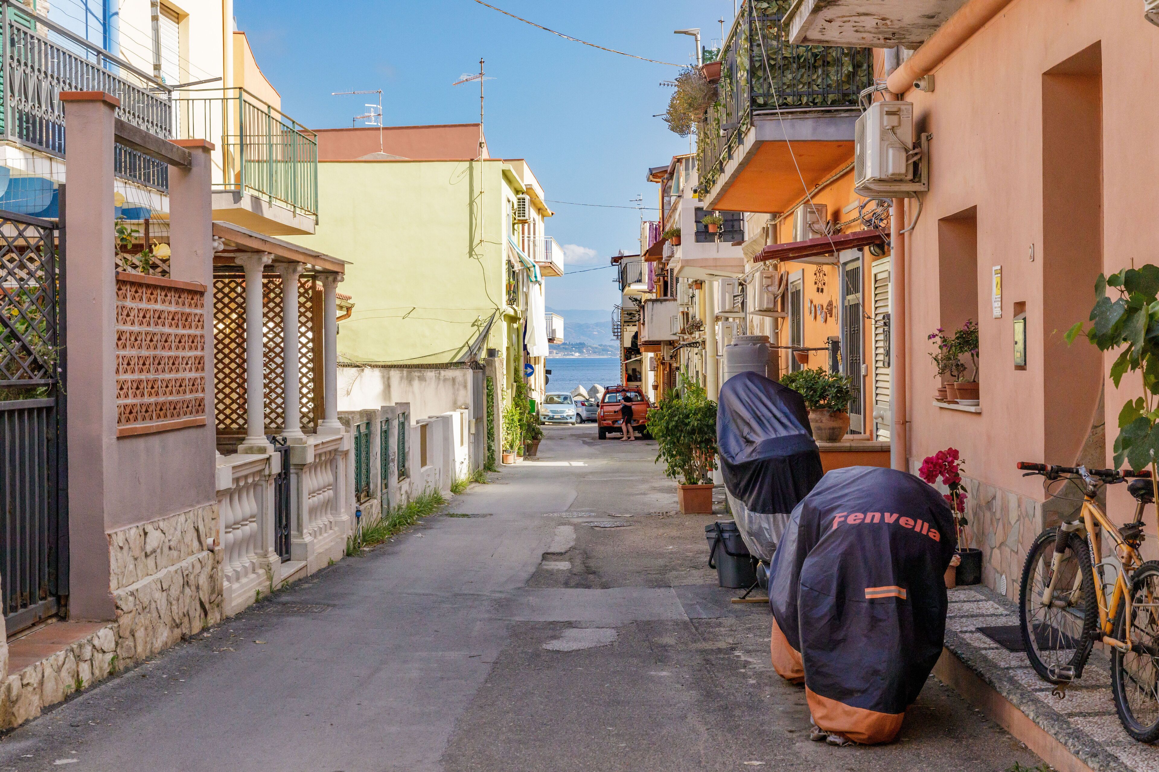A narrow street with buildings on both sides, a parked bicycle, and a person in a raincoat.