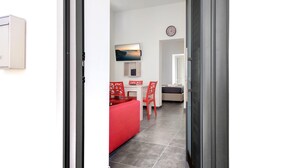 Un interior moderno con una zona de comedor que presenta un sofá rojo, una mesa blanca y sillas rojas. Un televisor de pantalla plana está montado en la pared sobre la mesa.