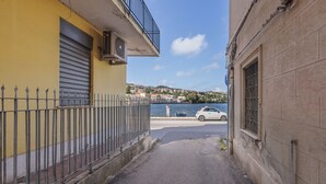 Un callejón estrecho con un edificio amarillo a la izquierda y uno beige a la derecha, que conduce a una masa de agua donde se puede ver un coche estacionado a la derecha.