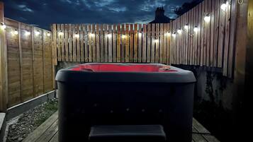 A hot tub in a wooden deck area with a wooden fence and string lights.