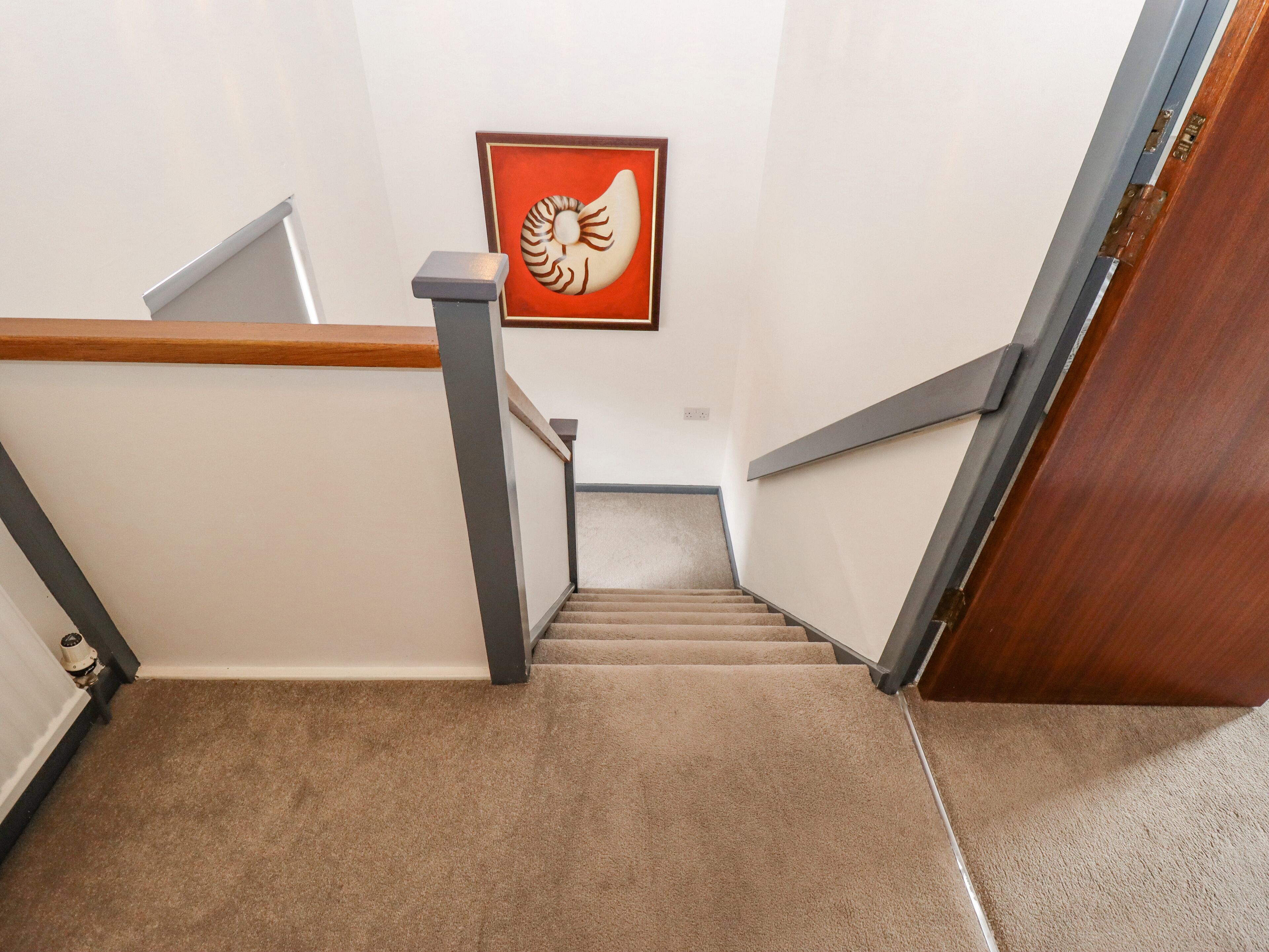Una escalera alfombrada con barandilla de madera y una obra de arte enmarcada en la pared.