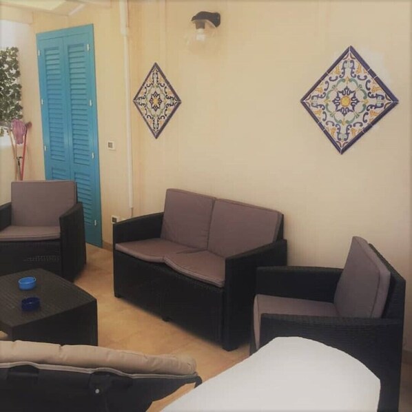 A room with a blue door, two armchairs, a sofa, a small table, and decorative wall tiles.