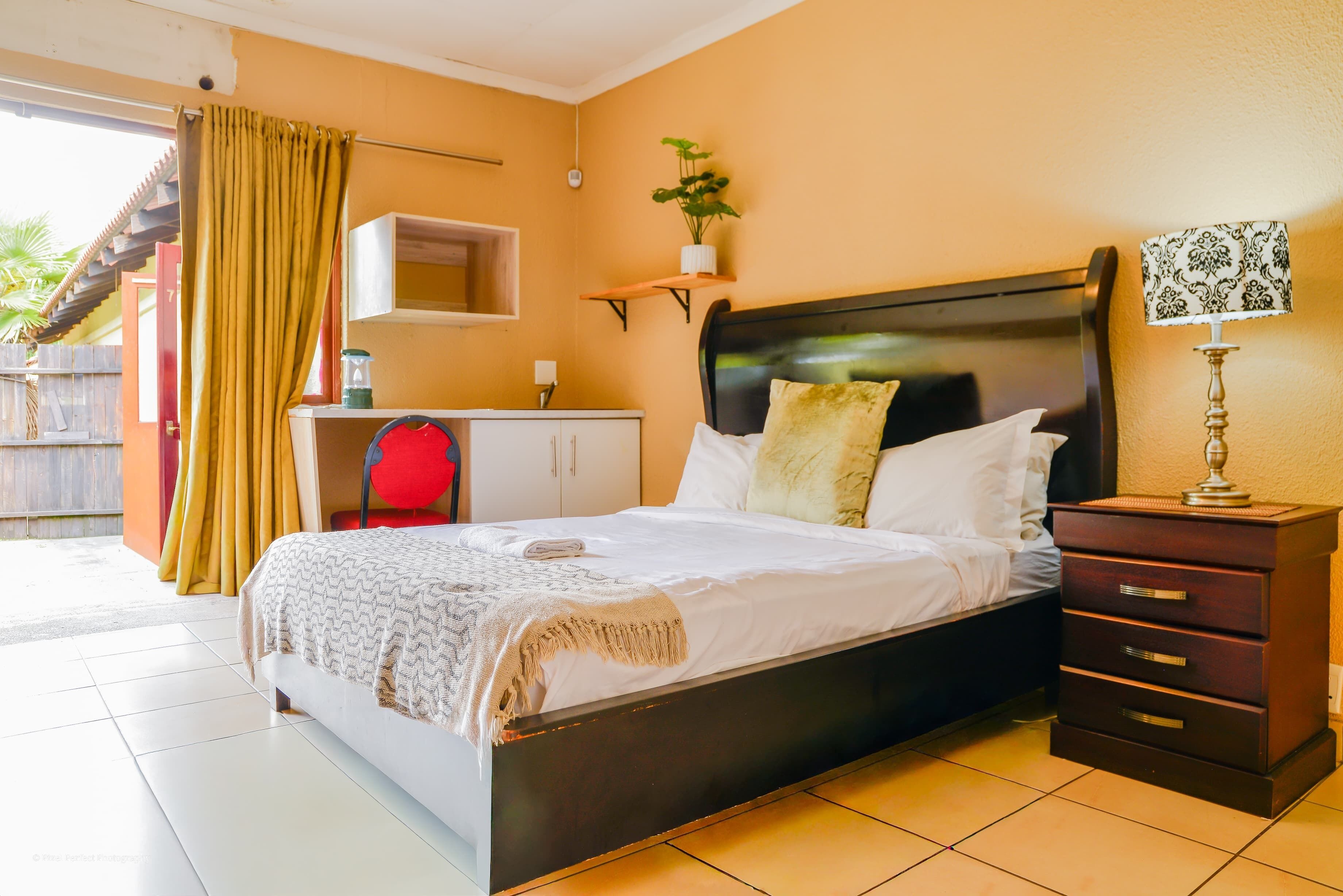 A bedroom with a bed, bedside table, lamp, and a small desk with a chair.