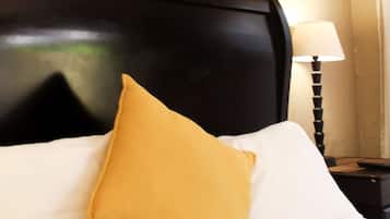 Una cama con cabecera negra, ropa de cama blanca y una almohada amarillo mostaza. Encima de la cama hay dos cuadros colgados en la pared.