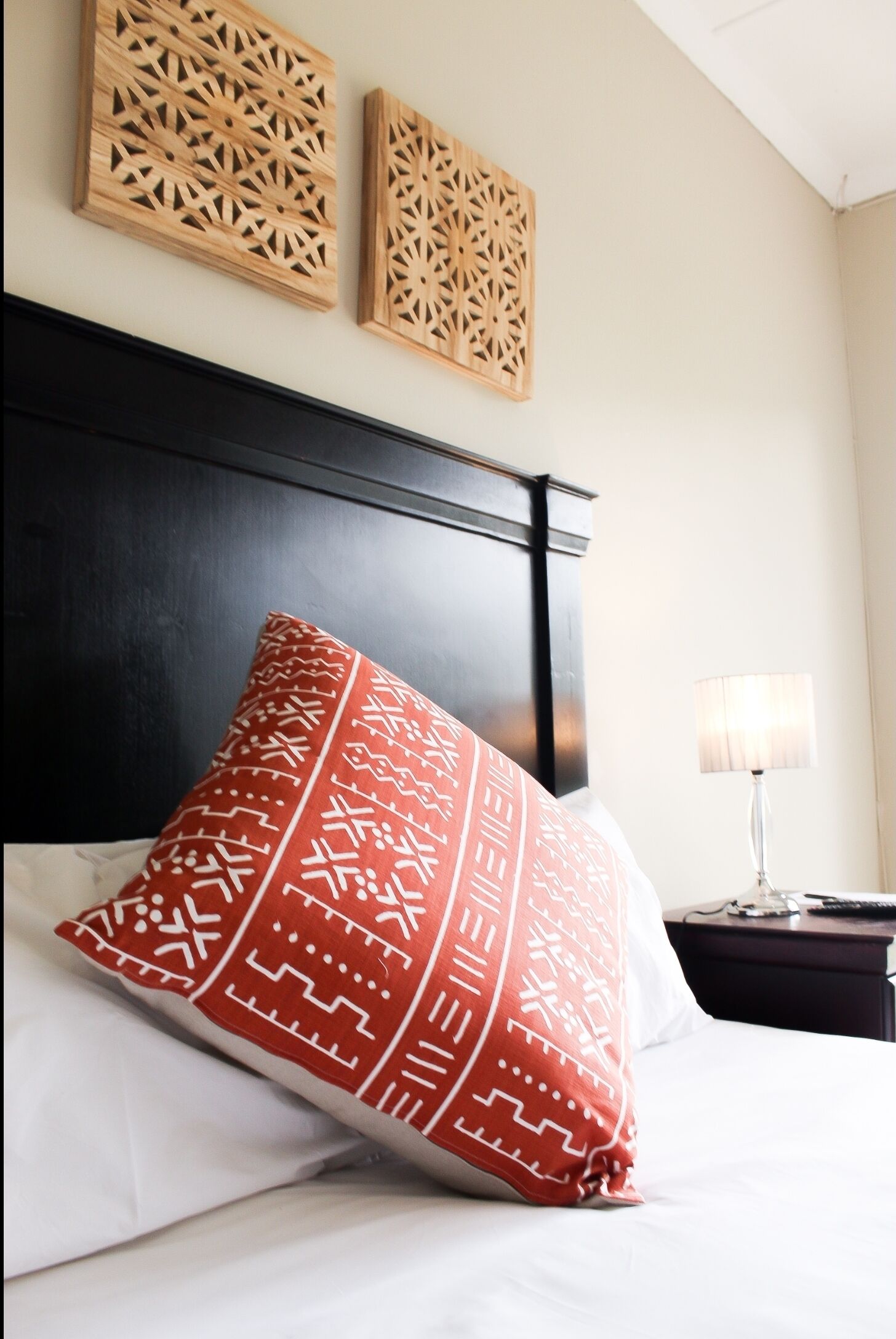 A neatly made bed with a patterned pillow, a dark headboard, and two wall-mounted wooden panels.