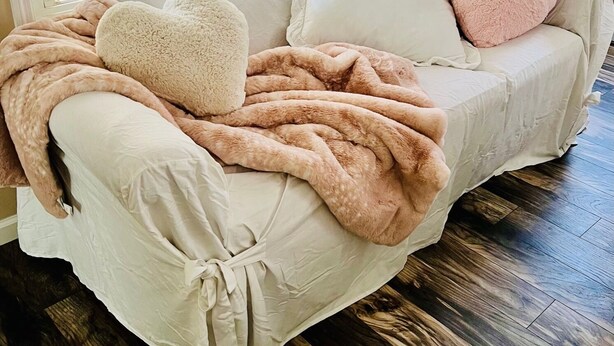 A cozy room with a white sofa adorned with a fluffy beige blanket and a pink heart-shaped pillow. - Coastal Casita by the River (New Bern)