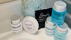 A bathroom sink with a glass bottle, a bar of soap, and several small bottles of Terra Pure body lotion. - Coastal Casita by the River (New Bern)