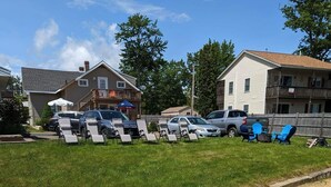 A residential area with a grassy lawn, a sandy area, and a row of parked cars.