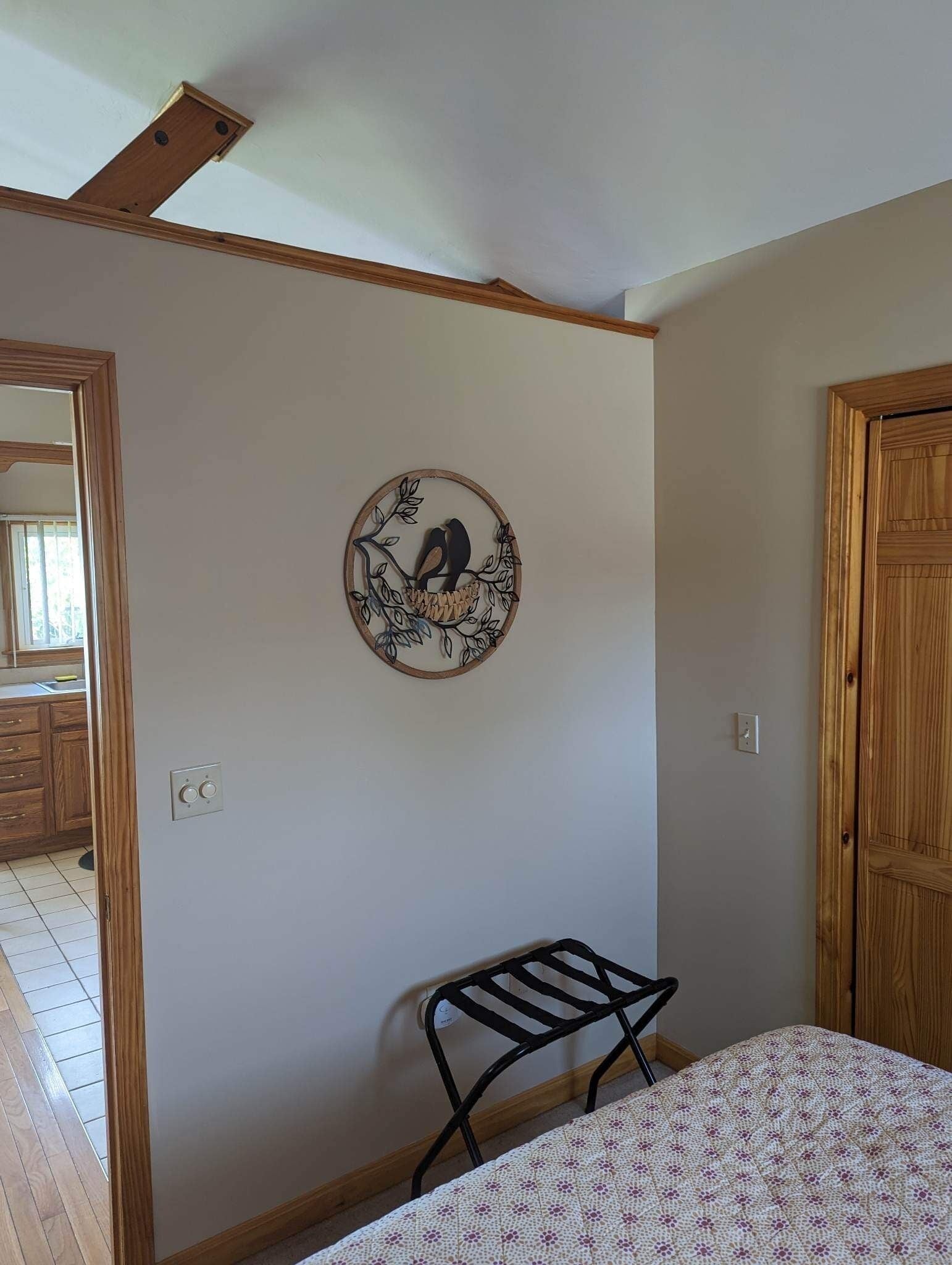 A room with a bed, a chair, a wooden door, and a wall-mounted decorative piece.