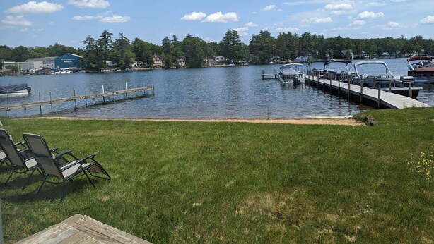 A lakeside view with a dock, boats, and a grassy area with chairs.