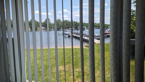 A view through a window with vertical blinds, overlooking a lake with boats docked at a pier.