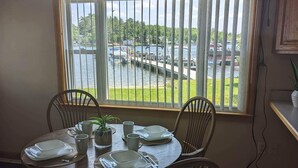 A dining area with a round table set for four, a potted plant, and a view of a marina with boats and a bridge.