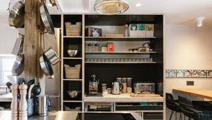 A modern kitchen with stainless steel appliances, wooden shelves, and a dining area with black chairs.