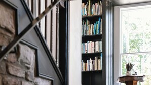 A staircase with a black railing and a brass sphere, a bookshelf filled with books, and a window with a view of trees.