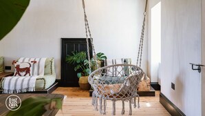 A cozy living room with a macramé swing chair, a sofa with patterned cushions, and a potted plant.