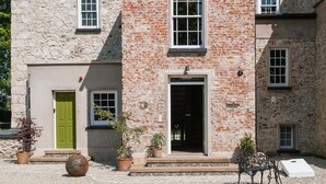 A stone building with a green door, a black entrance, and a gravel driveway.