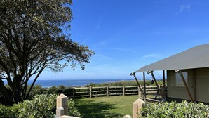 A wooden gate labeled "HANOIS" leading to a grassy area with a view of the sea and a building with a covered patio. - Seaside Serenity: Luxury Glamping Getaway - Sleeps 6 (St Peters)