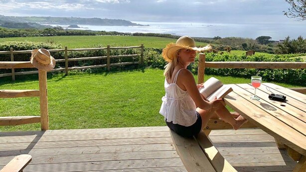 A person sitting at a wooden table with a view of a green field and the sea in the background. - Seaside Serenity: Luxury Glamping Getaway - Sleeps 6 (St Peters)