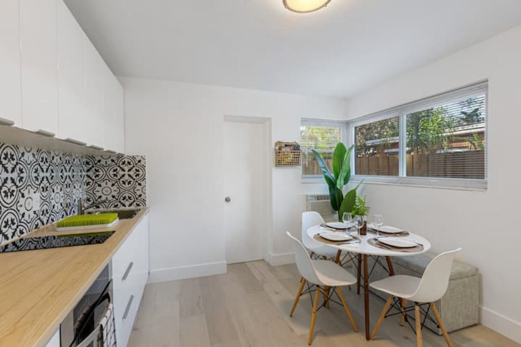 Une cuisine moderne avec des meubles blancs, un pare-feu décoré et un coin repas avec une table dressée pour quatre personnes.