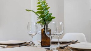 Une table à manger dressée avec des assiettes, des couverts et des verres à vin, agrémentée d’une plante décorative dans un vase.