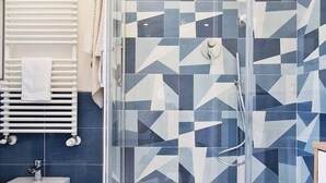 A bathroom with a shower area featuring geometric patterned tiles, a white sink, and a towel rack with towels. - Villa in Lemon Grove With Sea Views & Sea Breeze (Minori)