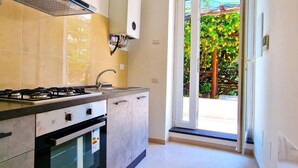 A kitchen with a gas stove, oven, and sink, a window with a view of greenery, and a sliding glass door to an outdoor area. - Villa in Lemon Grove With Sea Views & Sea Breeze (Minori)
