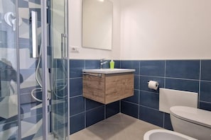 Une salle de bain moderne avec une douche à parois de verre, un meuble à pharmacie en bois, des toilettes blanches et un mur recouvert de carreaux bleus.