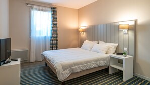 A hotel room with a bed, bedside table, lamp, and a TV on a stand.