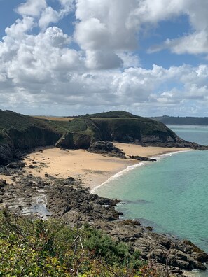 Eine Küstenlandschaft mit Sandstrand, felsiger Küstenlinie und Blick auf das Meer unter bewölktem Himmel.