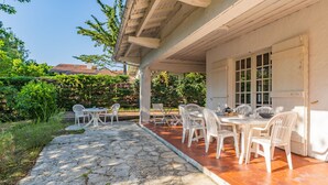 Eine überdachte Terrasse im Freien mit Steinböden und weißen Plastikstühlen.