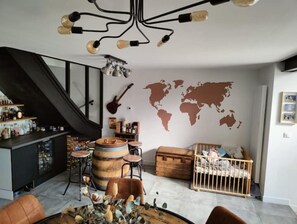 A modern living room with a world map on the wall, a guitar, and a rustic barrel. - Maison Familiale Avec Jardin (Ennevelin)