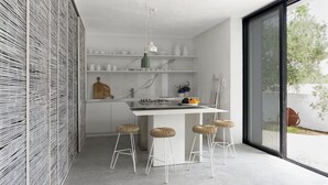 Una cocina moderna con armarios blancos, una isla central con taburetes y un ventanal con vistas al exterior.