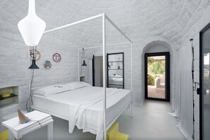 A bedroom with a four-poster bed, a bedside table, a lamp, and a view of the outdoors. - CocoTrullo (Ostuni)