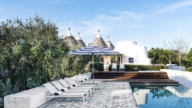 Zona junto a la piscina con sillones de descanso, una piscina y un edificio con tejados cónicos al fondo.