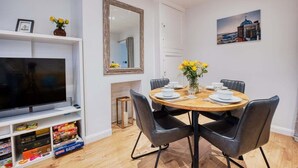 En matplats med ett runt bord, svarta stolar, en tv och en hylla med brädspel.