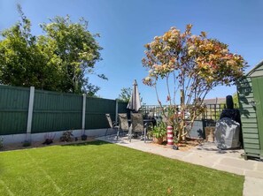 A backyard with a patio, a grill, and a green fence.