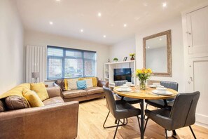 A modern living room with a sofa, dining table, chairs, a TV, and a large mirror.