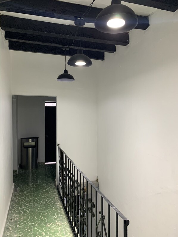 A hallway with a green patterned floor, a metal railing, and pendant lighting.