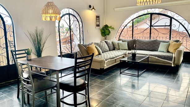 Una sala de estar con sofá, mesa de centro, mesa de comedor, sillas y dos lámparas colgantes.