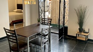Un comedor con una mesa y sillas, un colgador de luz y vista a través de un arco hacia un espacio exterior con valla de bambú.