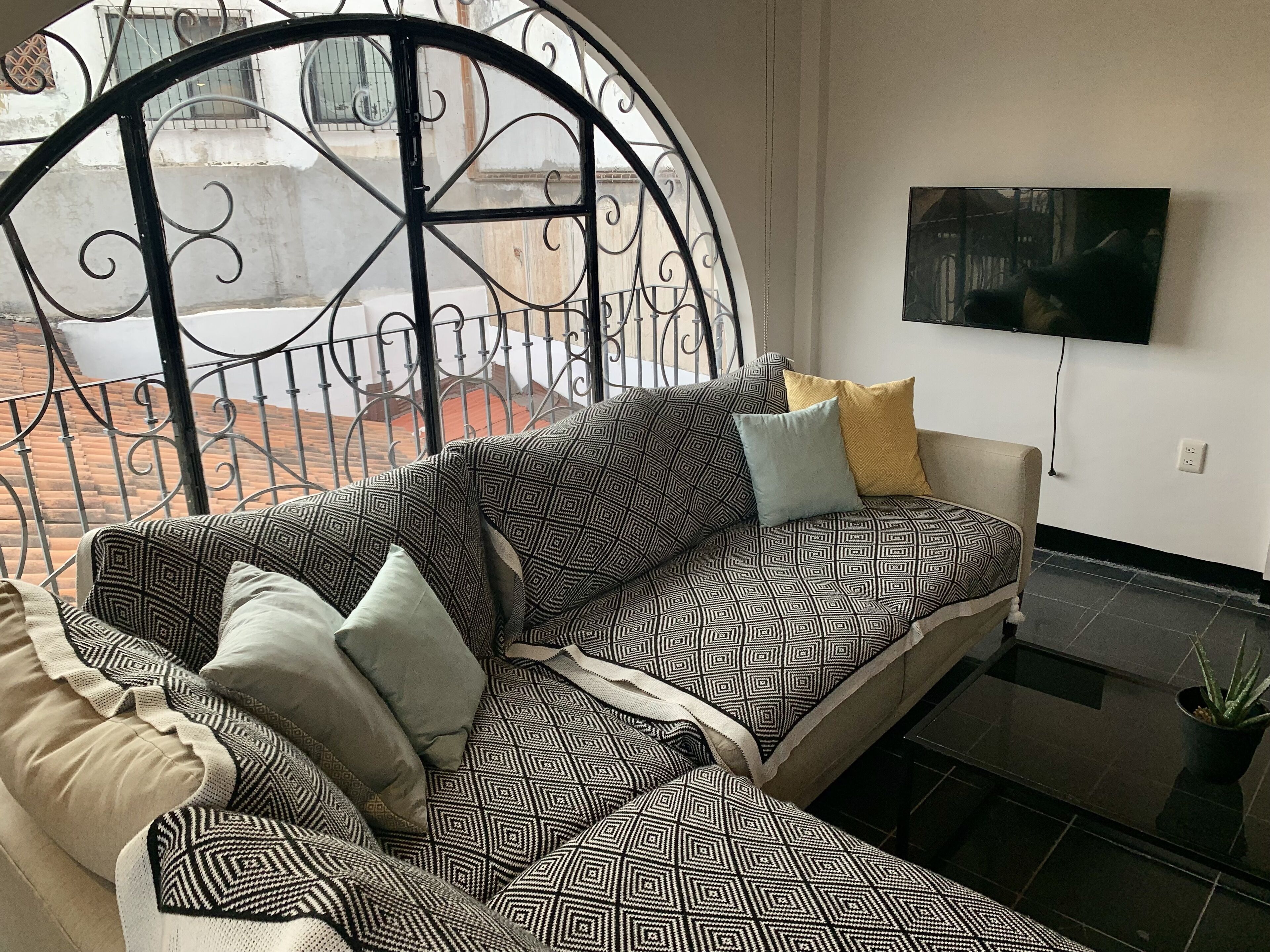 Una sala de estar moderna con un sofá estampado, un televisor de pantalla plana y vistas a un patio a través de una reja decorativa.