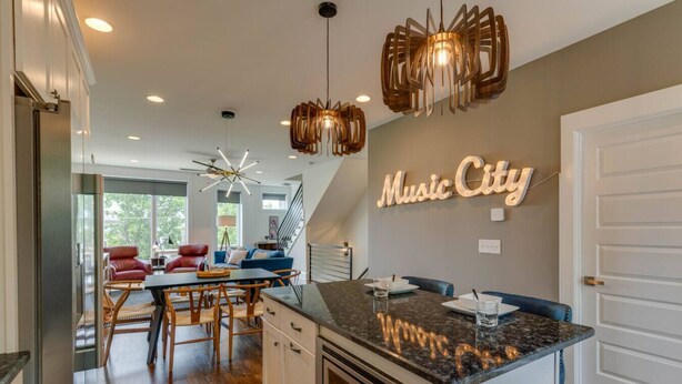 A modern kitchen with a marble countertop, a built-in oven, and a dining area with a red leather chair and a blue sofa. - Melrose Townhome Balcony|Walkable to Coffee & Eats (Berry Hill)