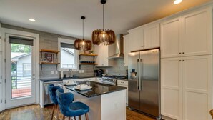 A modern kitchen with white cabinets, a stainless steel refrigerator, and a central island with bar stools. - Melrose Townhome Balcony|Walkable to Coffee & Eats (Berry Hill)