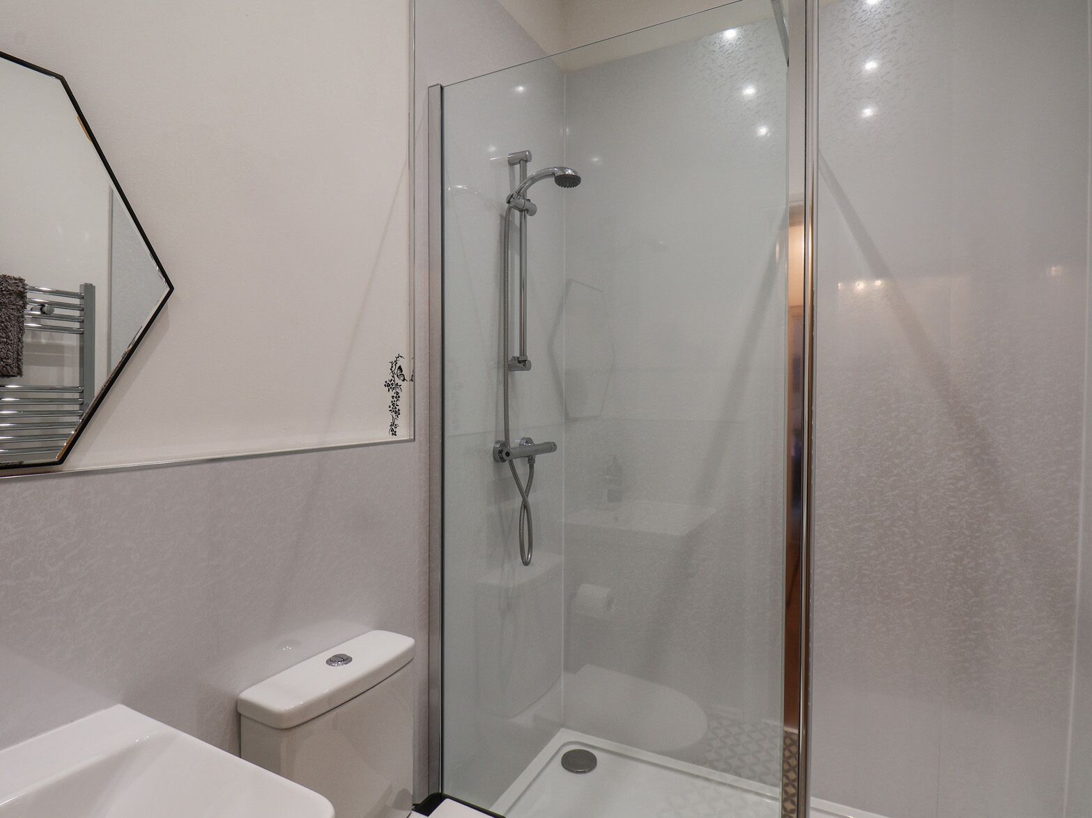 A modern bathroom with a glass-enclosed shower, a white toilet, and a mirror with a decorative frame.