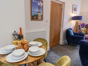 A dining area with a table set for breakfast, including croissants, plates, and a coffee pot.