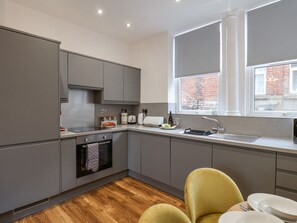 A modern kitchen with grey cabinets, a built-in oven, a sink, and a window with a view of a brick building.