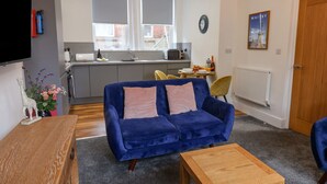 A modern living room with a blue sofa, a wooden coffee table, and a kitchen in the background. - Routh Retreat (Whitby)