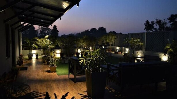 Un patio al aire libre con plantas en macetas y una terraza de madera, iluminado con luz ambiental.