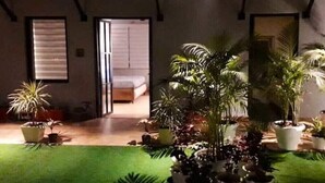 Una habitación con una cama, una puerta que da a otra habitación y un pequeño jardín interior con diversas plantas.